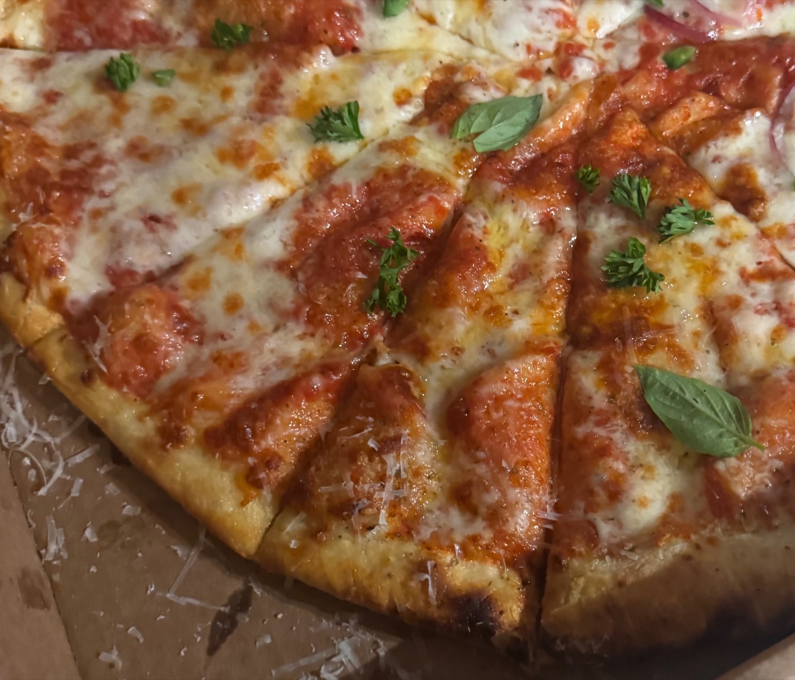 A sliced cheese pizza topped with parsley, basil, and grated parmesan