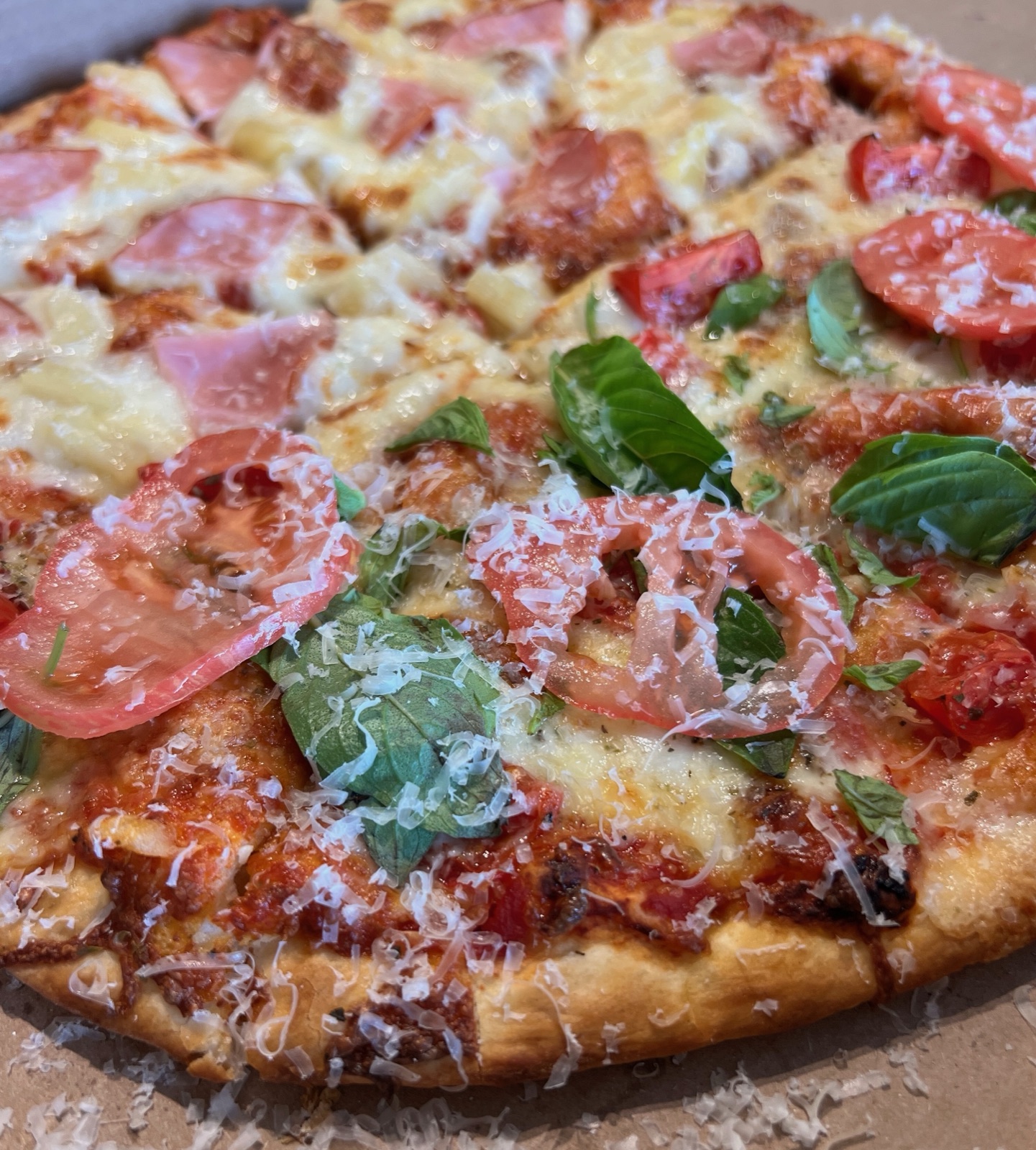 A half-and-half pizza, ham and pineapple on one side and tomato and basil on the other, dusted with parmesan