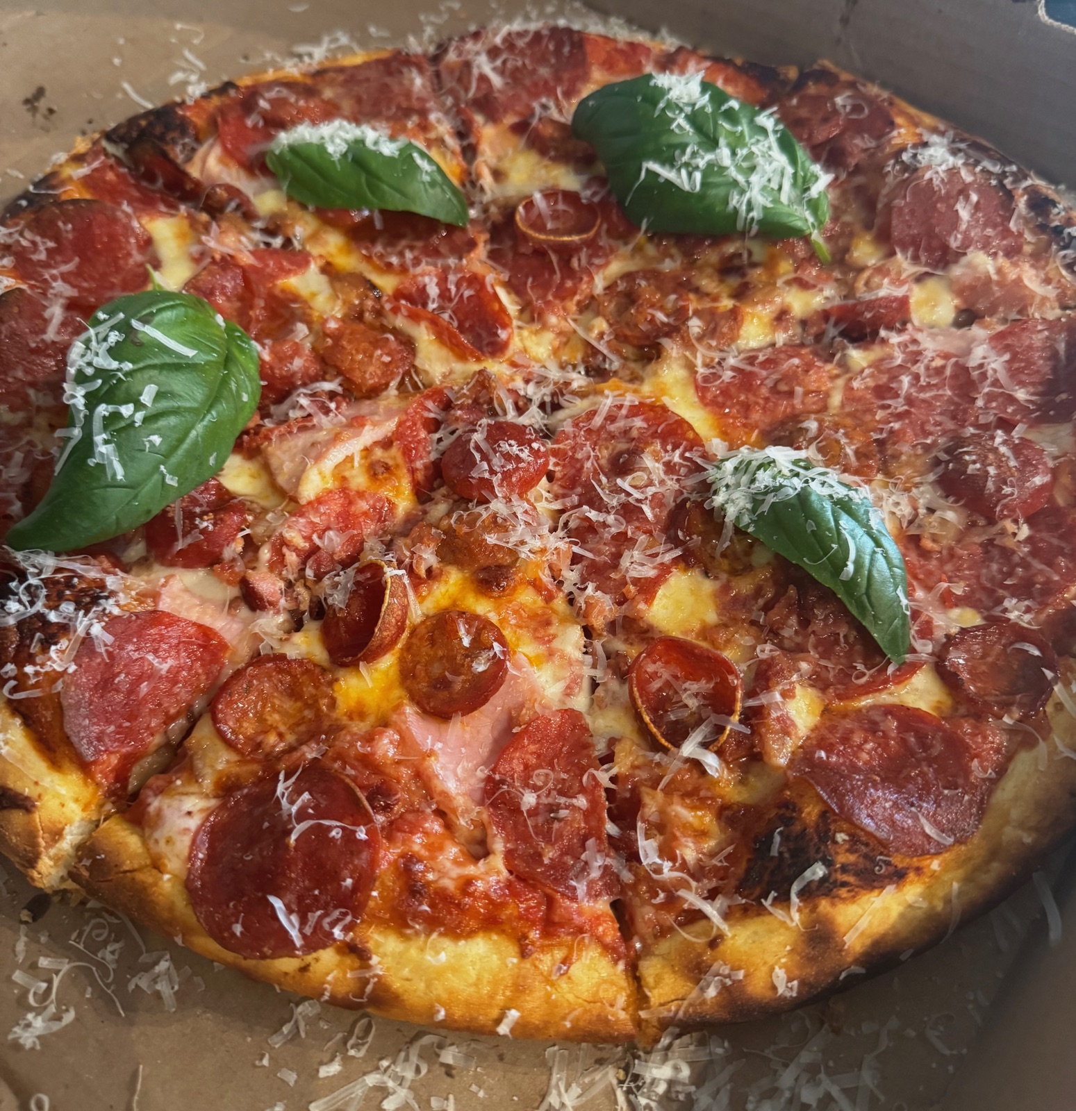 A whole pepperoni pizza with fresh basil leaves and a heavy dusting of parmesan