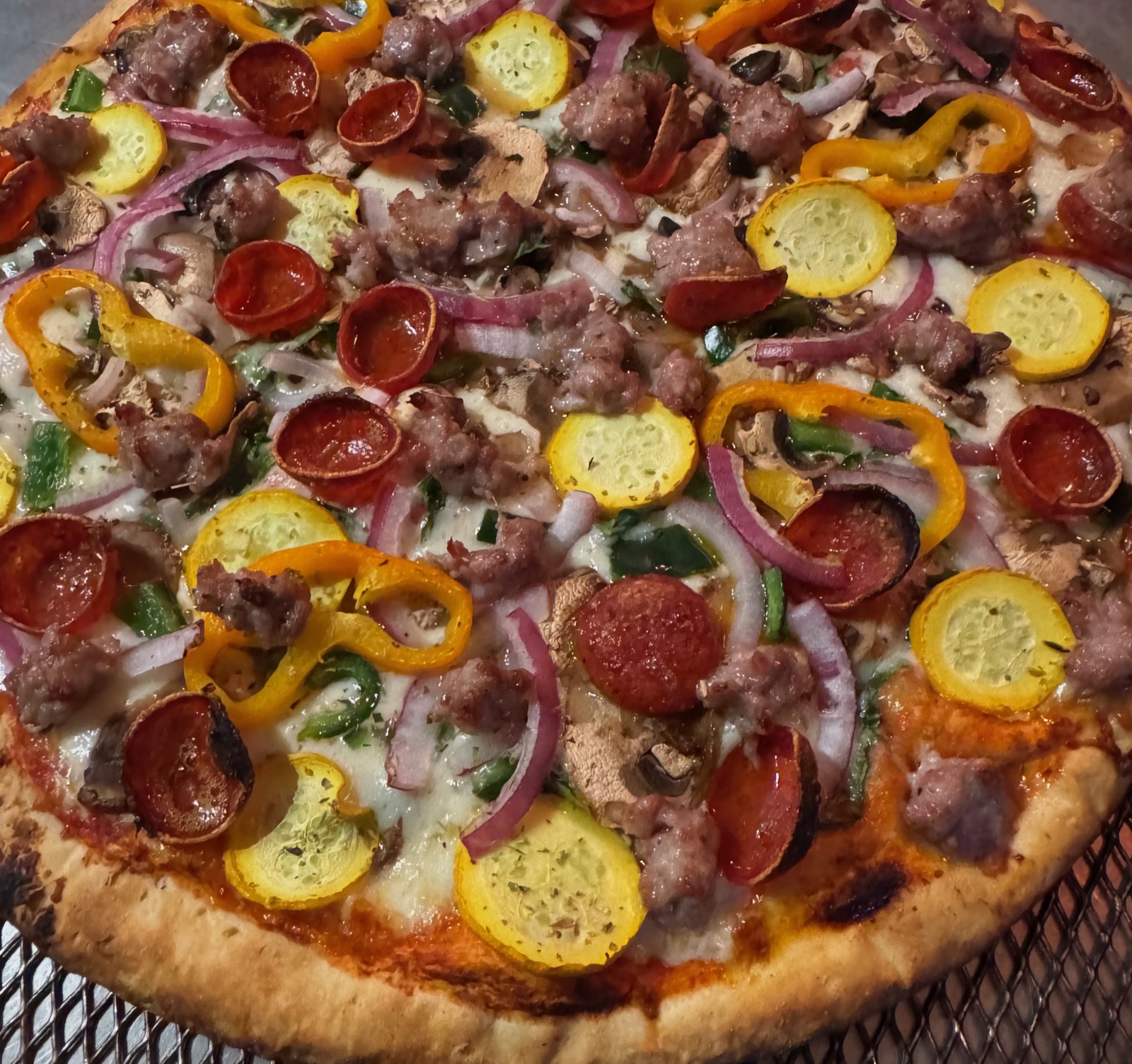 A whole pizza topped with pepperoni, sausage, peppers, onion, and squash
